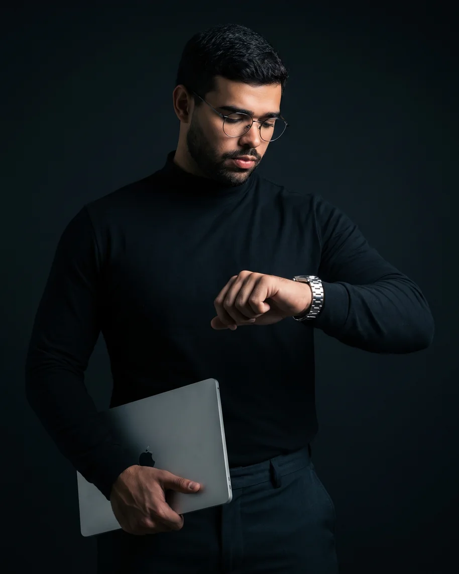 Gabriel Braz de blusa preta, segurando o notebook e olhando o relógio
